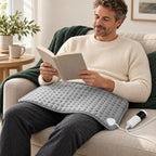 Grey model 406 heating pad resting over clothing across the lap of an awake adult reading at home