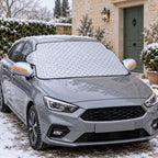 Silver quilted no-strap windscreen cover fitted to a parked grey car on a winter morning