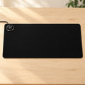 Black AI heated desk mat with integrated round digital controller on a pale oak desk