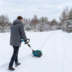 A man guiding a teal cordless snow sweeper along a snow-covered outdoor path